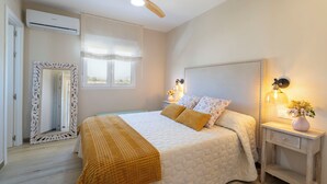 A bedroom with a bed, a ceiling fan, an air conditioning unit, a mirror, a window with curtains, bedside lamps, and a nightstand with a vase of flowers. - LUXURY VILLA PARAISO ALICANTE—Heated saltwater pool, fireplace, gym, Netflix (Monforte del Cid)