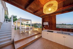 A modern kitchen with a large window, a dining area with outdoor seating, and a staircase leading to an upper level.