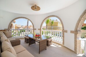 A balcony with a sofa, table, and chairs, overlooking a residential area.