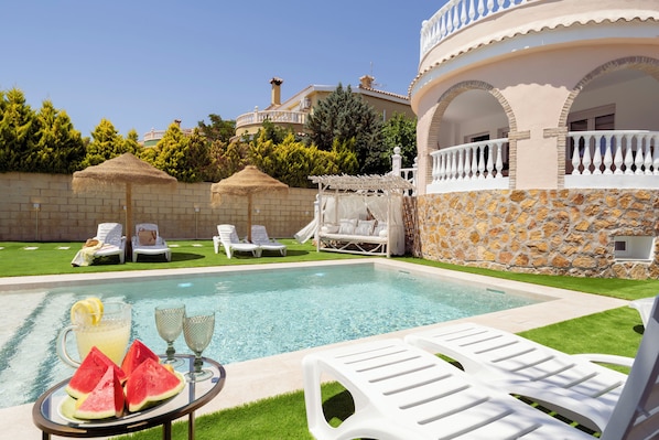 A poolside area with lounge chairs, a table with fruit and drinks, and a stone wall.
