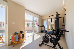 A spacious room with a ceiling fan, a treadmill, and a window overlooking a balcony with outdoor furniture.