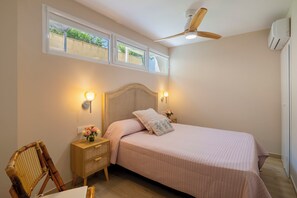 A bedroom with a bed, bedside lamps, a nightstand, a chair, a ceiling fan, and a window.
