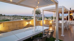 An outdoor patio with a long table and chairs, a brick wall, and a view of the landscape. - LUXURY VILLA PARAISO ALICANTE—Heated saltwater pool, fireplace, gym, Netflix (Monforte del Cid)