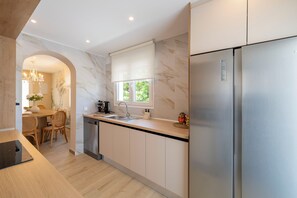A modern kitchen with a stainless steel refrigerator, a window with a view, and a dining area with a chandelier.