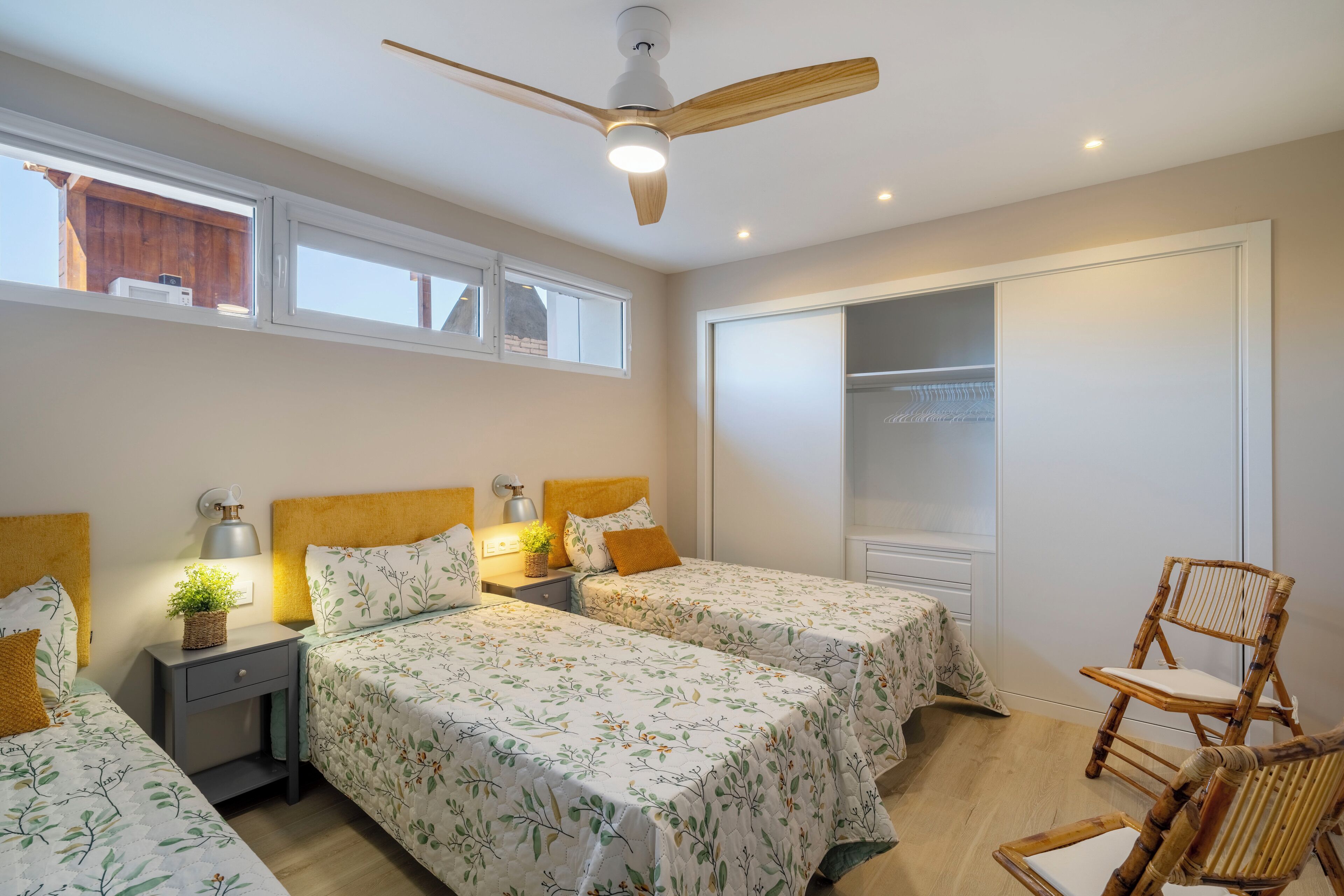 Un dormitorio con dos camas, ventilador de techo, armario y una silla.