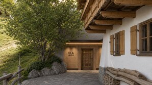 A building with a wooden facade, a stone pathway leading to a door marked 'ULA signature,' and a rustic wooden fence.