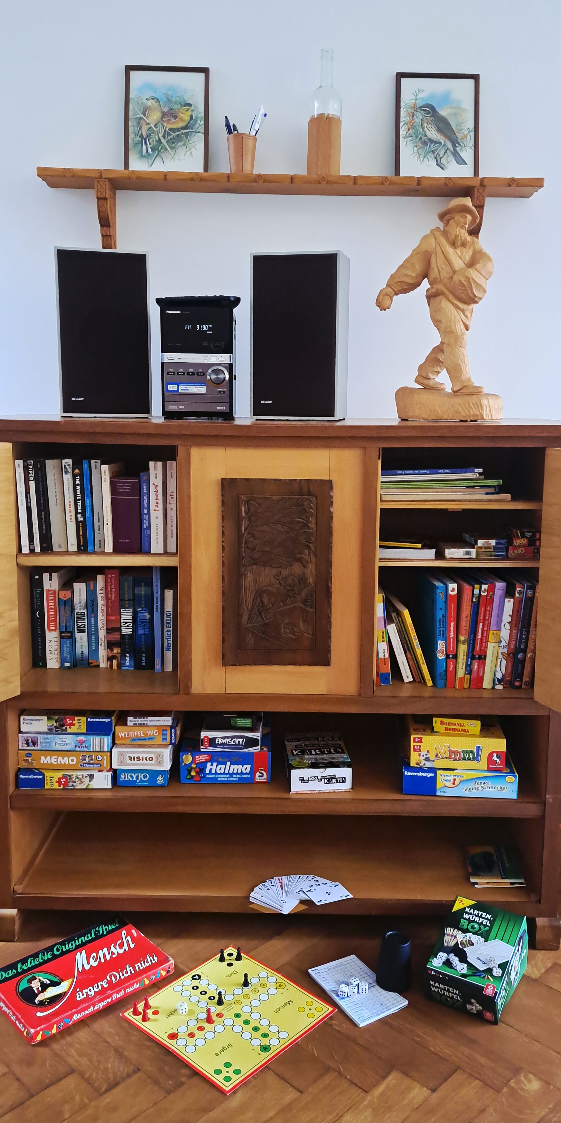 Ein Zimmer mit einer Holzhülle voller Bücher und Brettspielen, einem kleinen Tisch mit einem Brettspiel und einer Holzskulptur.