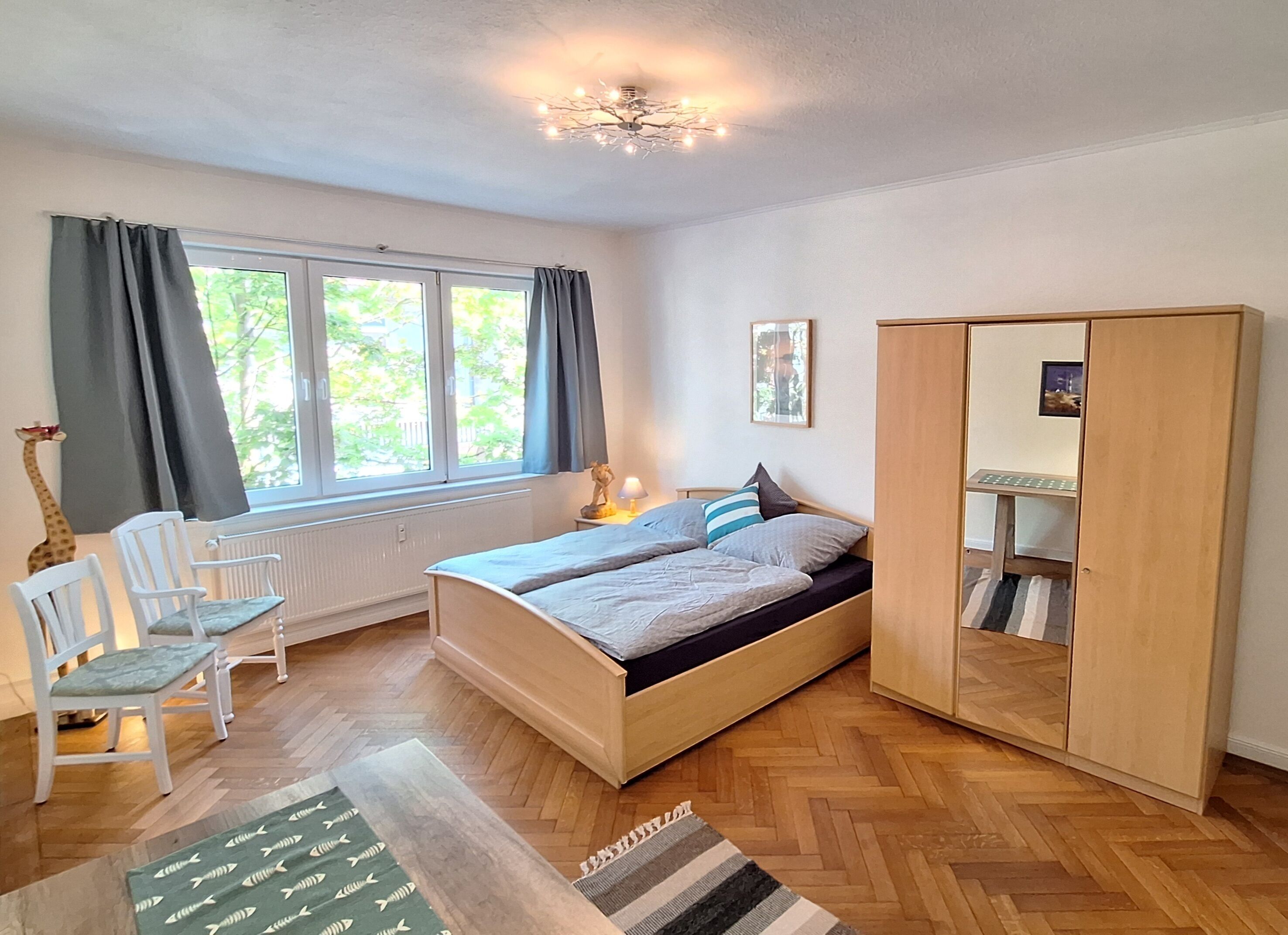 A bedroom with a bed, a wardrobe, a chair, a radiator, and a window with curtains.