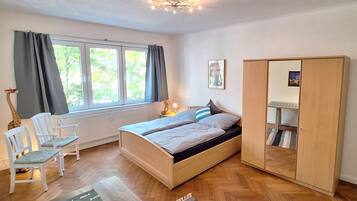 A bedroom with a bed, a wardrobe, a chair, a radiator, and a window with curtains.