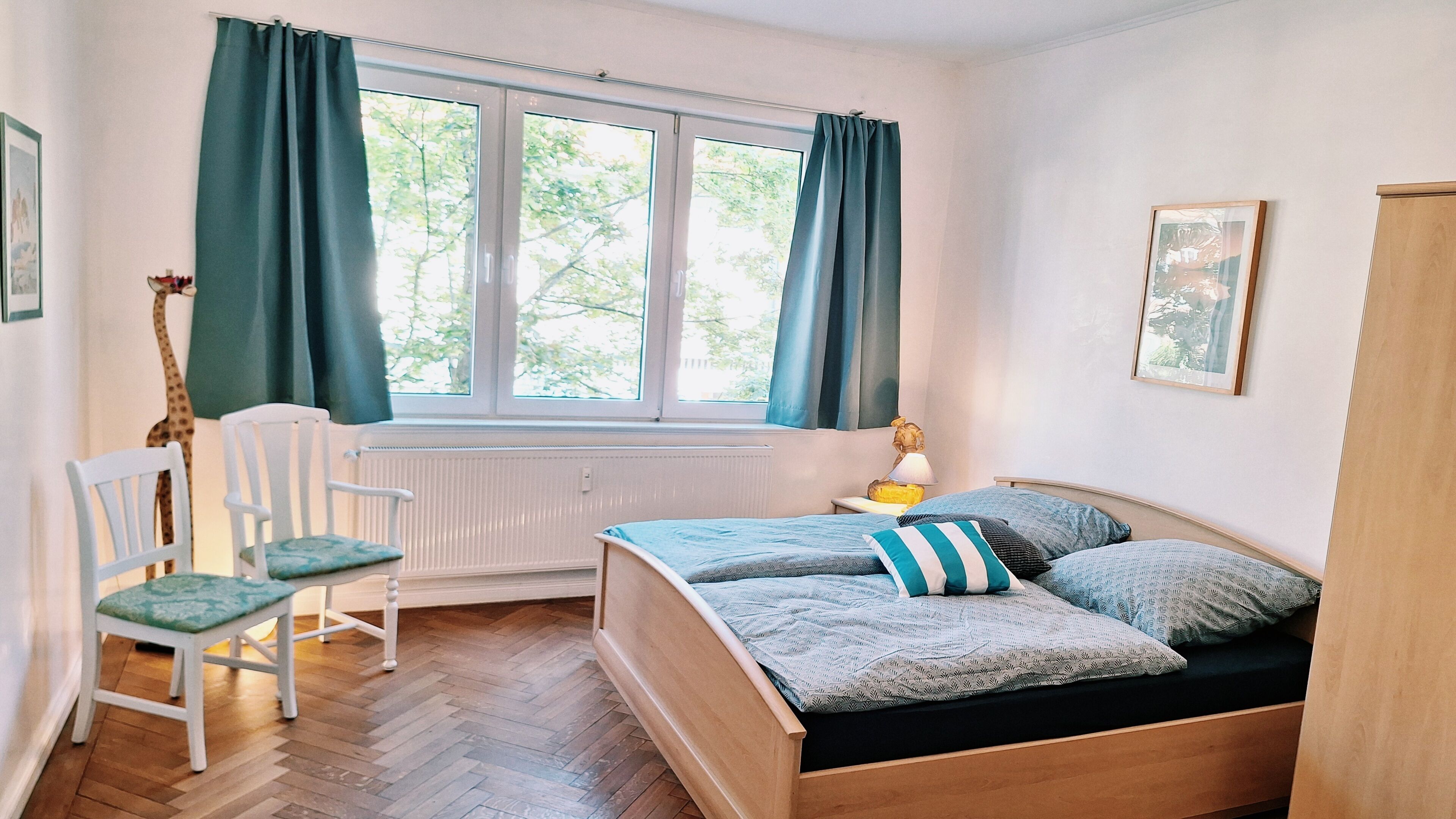 Una habitación con cama, una silla, ventana con cortinas, un radiador y una lámpara.