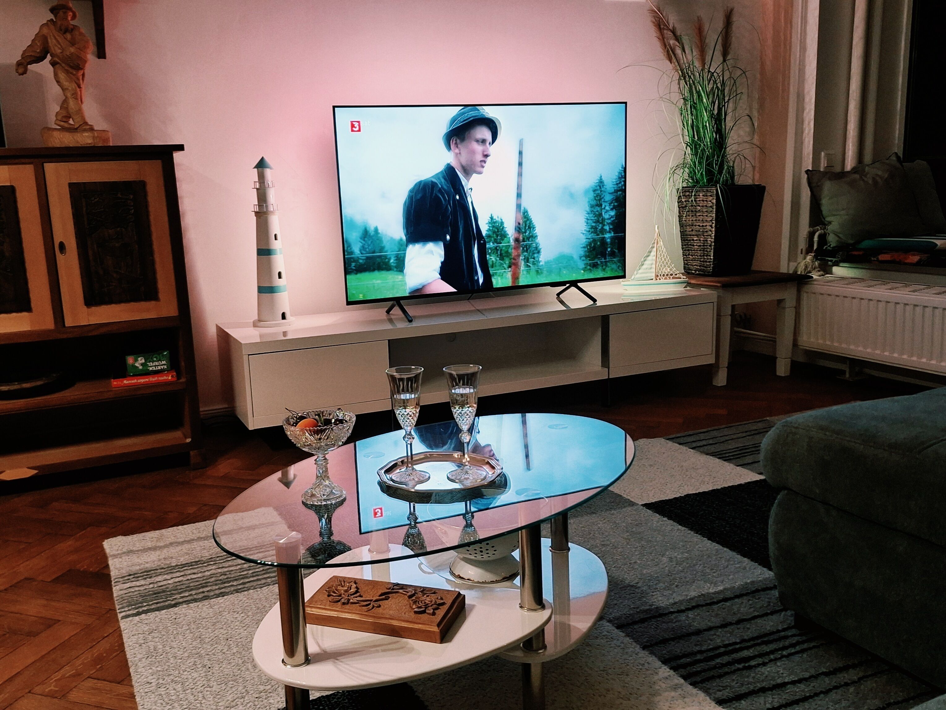 A living room with a television on a stand, a glass coffee table with decorative items, and a statue on a cabinet.