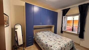 A bedroom with a bed, a wardrobe, a mirror, and a window with curtains.