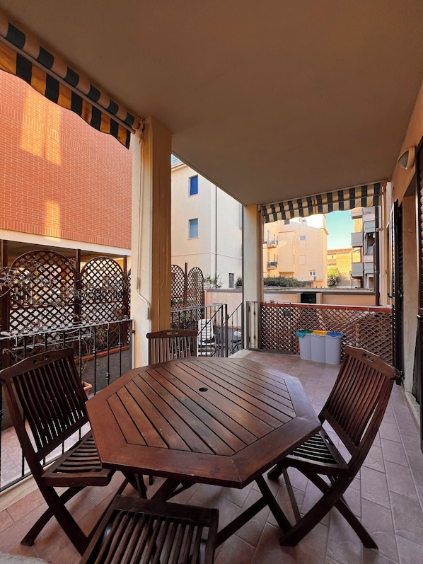 Un patio al aire libre con una mesa y sillas de madera, una valla de metal y vistas de edificios al fondo.