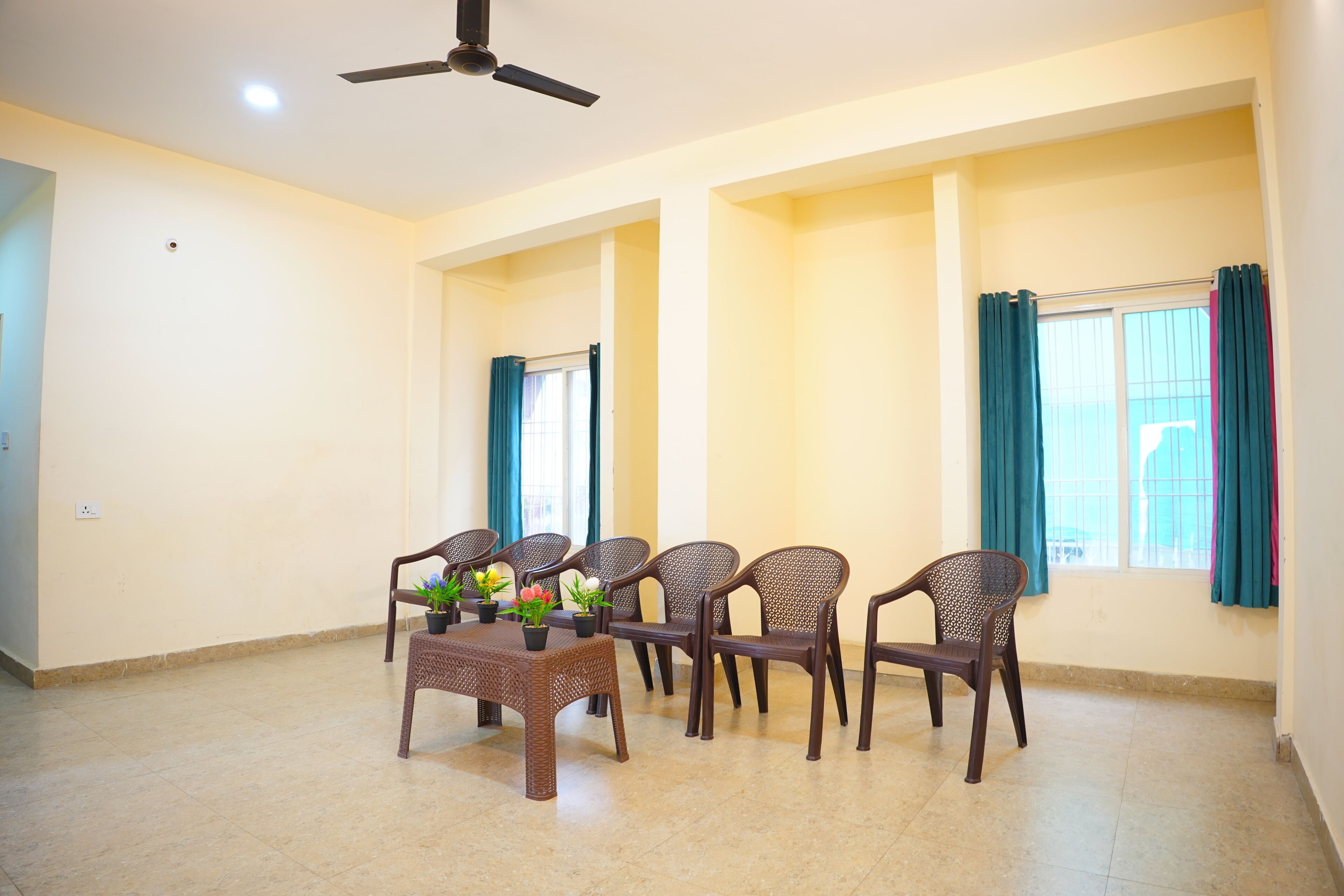A spacious room with a ceiling fan, a dining table with chairs, and a window with curtains.