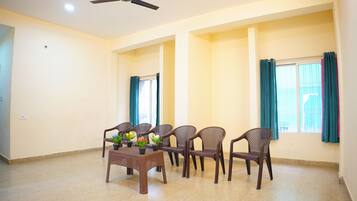 A spacious room with a ceiling fan, a dining table with chairs, and a window with curtains.