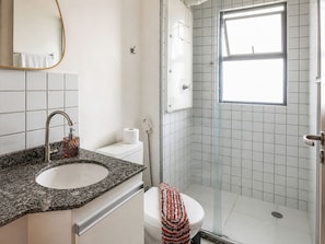 Ein Badezimmer mit Marmorwaschtisch, Toilette, Duschkabine mit Glastür und einem Fenster für natürliches Licht.