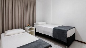 A hotel room with two beds, a nightstand, a ceiling fan, and a window with curtains. - CJC Short Stay Ecogarden (Natal)