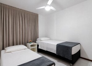 Ein Hotelzimmer mit zwei Betten, einem Nachttisch, einem Deckenventilator und einem Fenster mit Vorhängen.