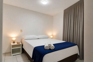 Ein Hotelzimmer mit einem Bett, zwei Nachttischlampen, einem Nachttisch, einem zusammengerollten Handtuch auf dem Bett und einem Vorhang.