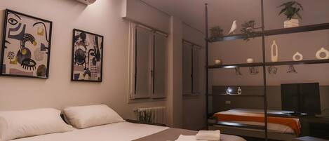 A modern hotel room with a large bed, a desk, and a shelving unit with decorative items.
