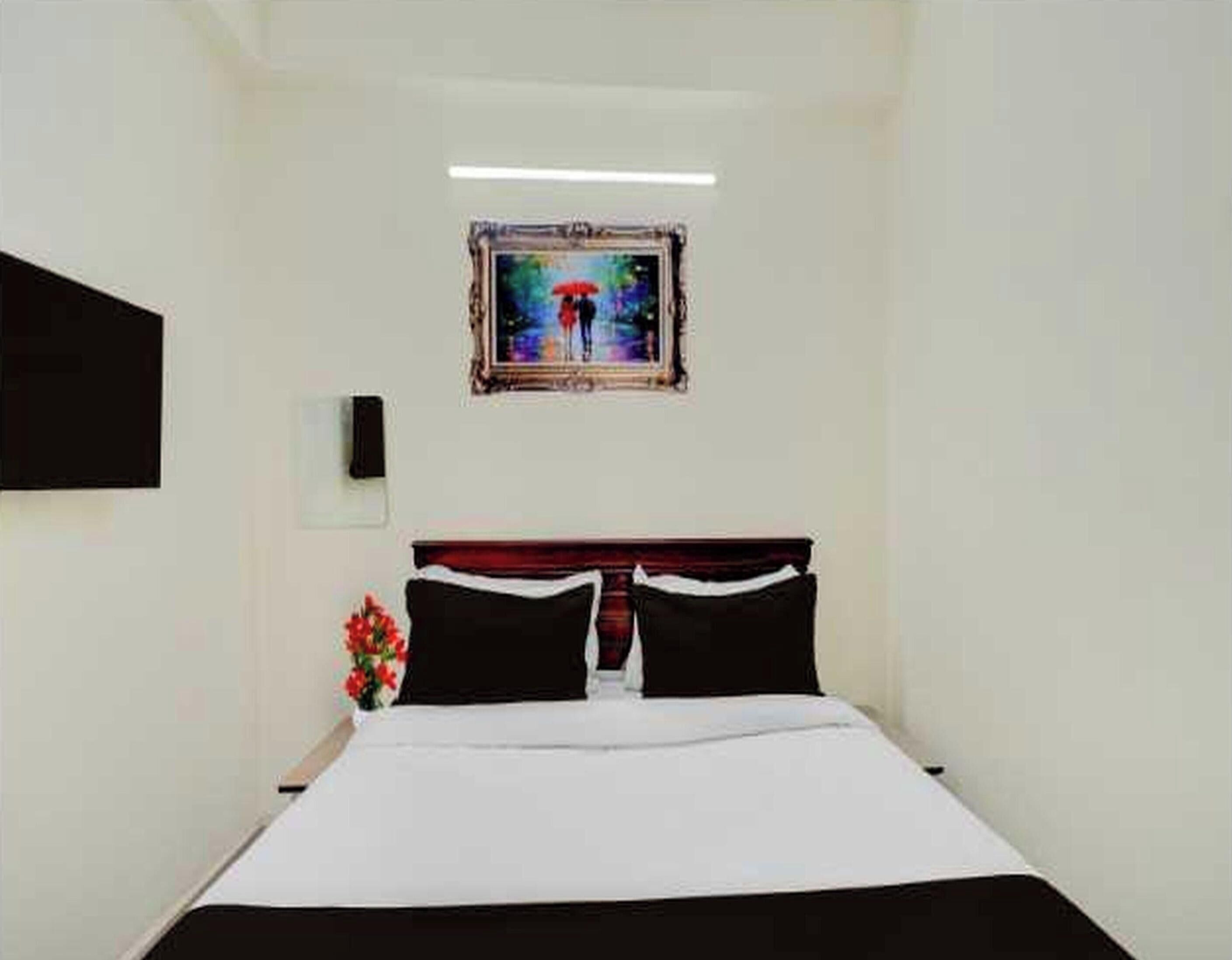 Ein Hotelzimmer mit einem Bett, einem Bild von zwei Personen unter einem Regenschirm, einem Nachttisch und einem an der Wand montierten Fernseher.