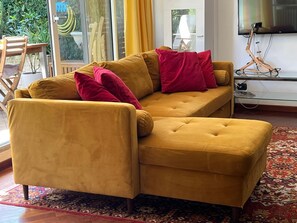 A mustard-colored sofa with red cushions in a room with a large window, a television, and a patterned rug. - Lake of Varese, "Residenza Mirabella" (Gavirate)