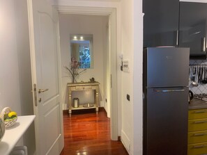 A kitchen with a refrigerator, wooden flooring, and a window with curtains.