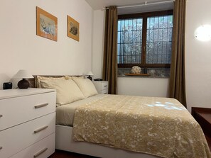 Ein Schlafzimmer mit einem Bett, Nachttischen, einer Kommode und einem Fenster mit Vorhängen.