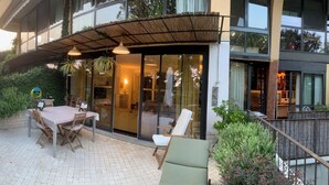 Eine Terrassensitzgelegenheit im Freien mit Esstisch und Stühlen, einem überdachten Sitzbereich und Blick ins Innere durch Glastüren.