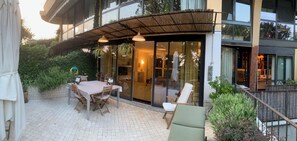 Eine Terrassensitzgelegenheit im Freien mit Esstisch und Stühlen, einem überdachten Sitzbereich und Blick ins Innere durch Glastüren.