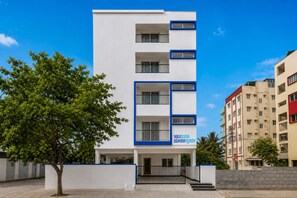 Un edificio de varios pisos con fachada blanca y detalles azules, que cuenta con balcones y una entrada a nivel de calle.
