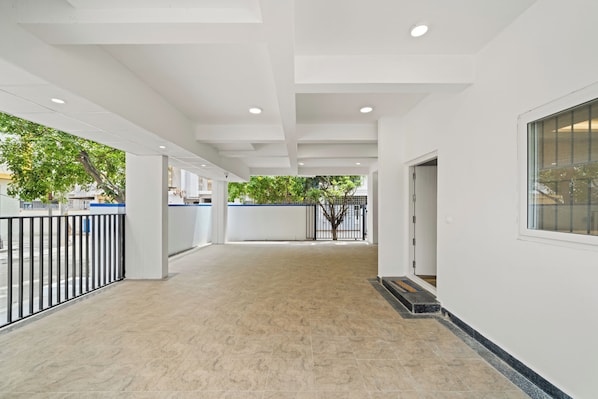 A spacious corridor with a tiled floor, white walls, and a metal fence on one side.