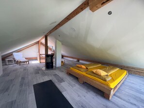 A room with a sloped ceiling, a bed with yellow bedding, a small table, and a chair. - Panoramic view (Stiefenhofen)