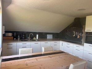 A compact kitchen with a dining table, white cabinets, and a black range hood. - Panoramic view (Stiefenhofen)