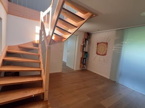A wooden staircase leading to a landing, a bookshelf, and a wall with a geometric design. - Panoramic view (Stiefenhofen)