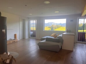 A spacious room with a large window, a sofa, a small table, and a refrigerator. - Panoramic view (Stiefenhofen)
