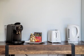 Een koffiezetapparaat, een doos koffiepads, een broodrooster en een waterkoker op een houten tafel.