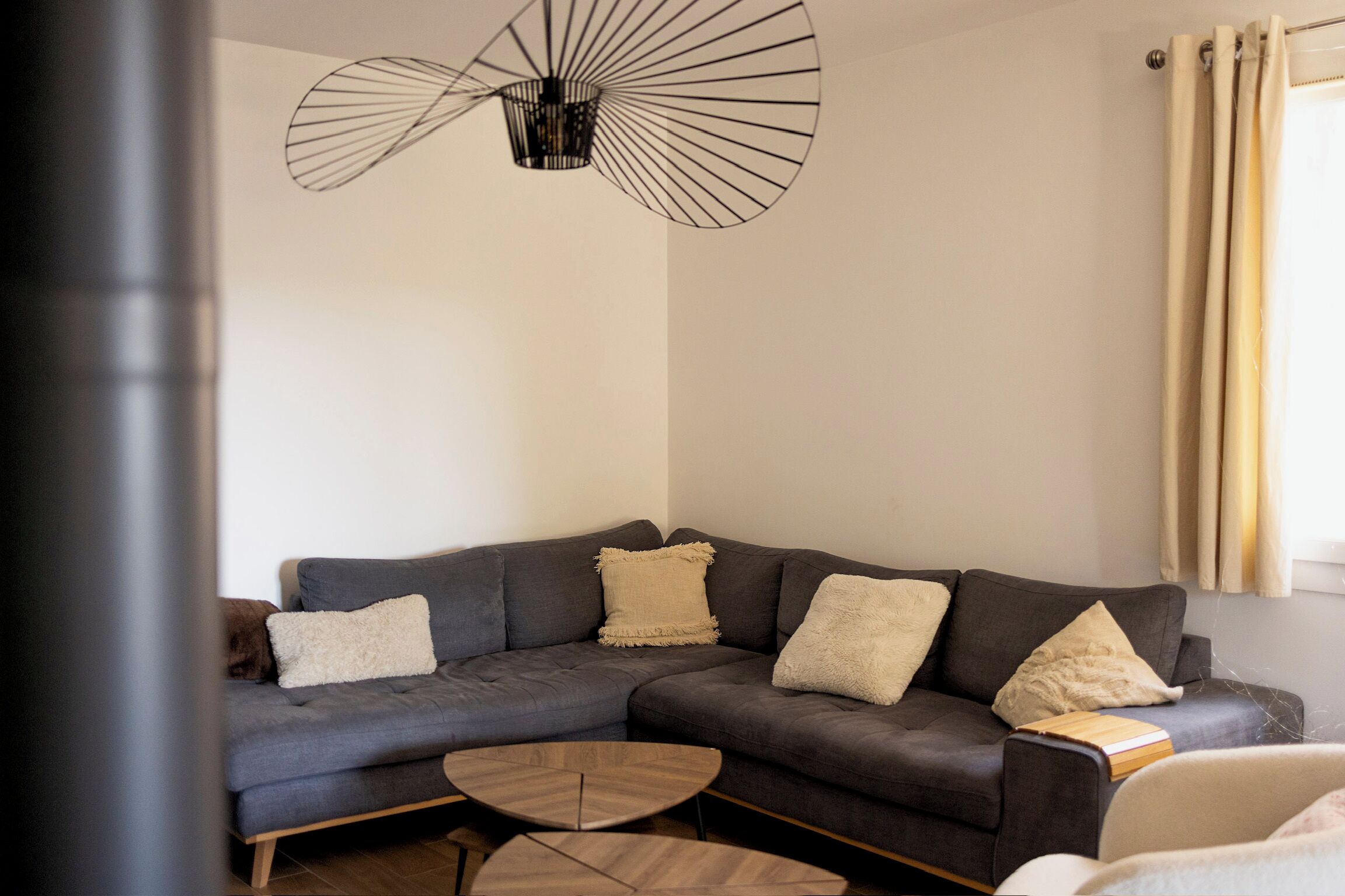A modern living room with a grey sectional sofa, a wooden coffee table, and a unique pendant light.