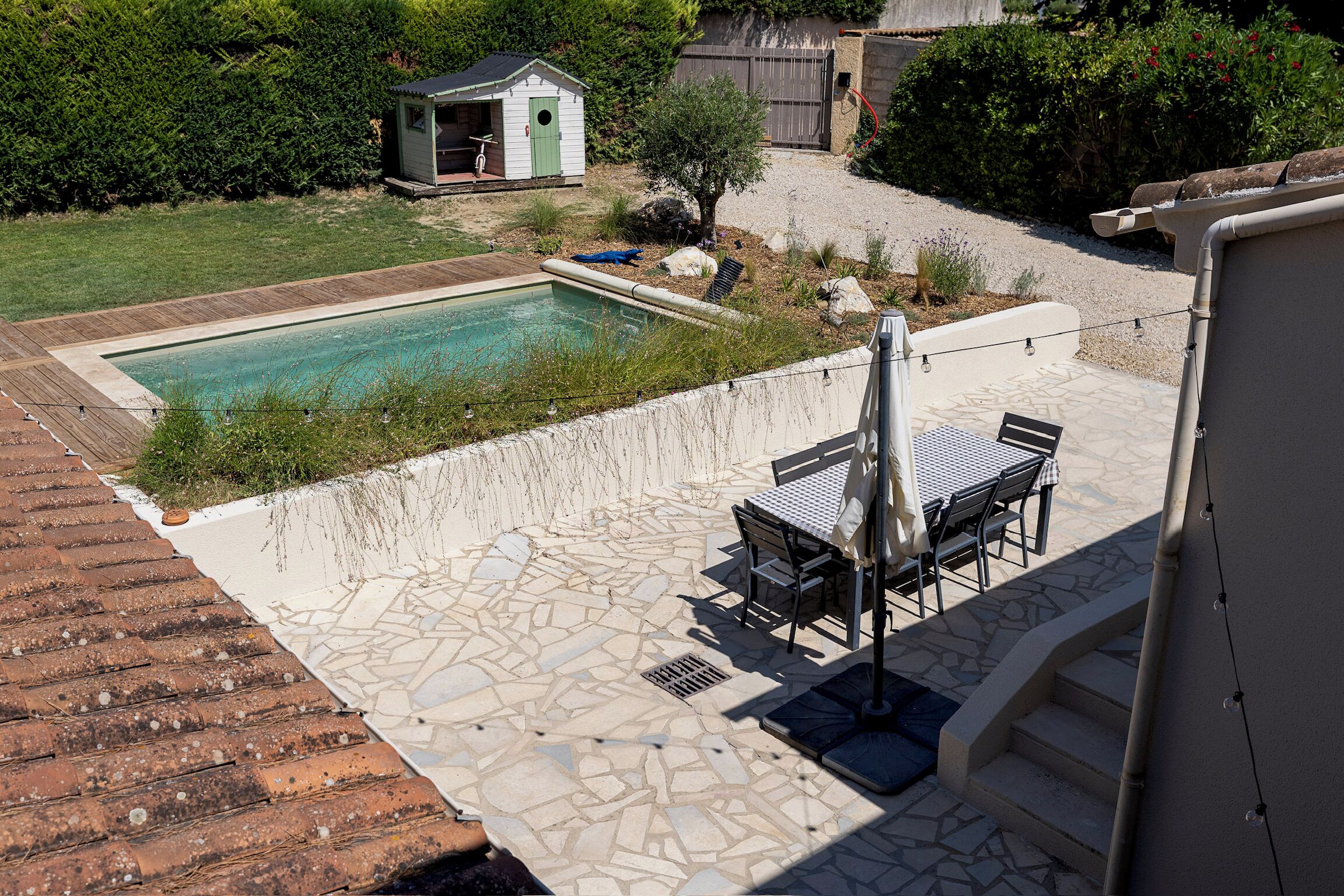 En swimmingpool med en terrasse, et lille skur og en have.