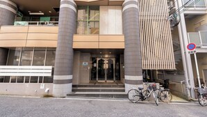 Um edifício moderno com entrada de vidro, pilares grandes e um aviso de proibido estacionar.