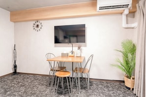 A room with a wooden ceiling, a mounted flat-screen TV, a table with chairs, a potted plant, and a wall clock. - b&Dotonbori 1 (Chuo Ward)