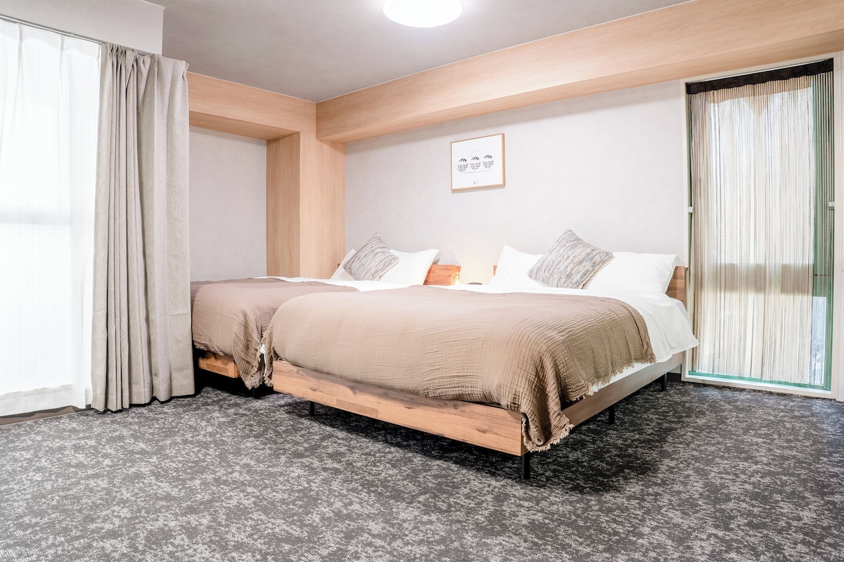 A hotel room with a wooden bed, a large window with curtains, and a framed picture on the wall.