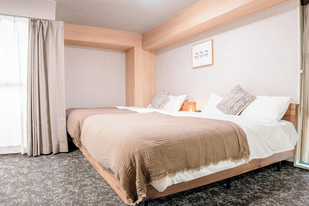 A hotel room with a bed, a window with curtains, a framed picture on the wall, and a textured carpet.