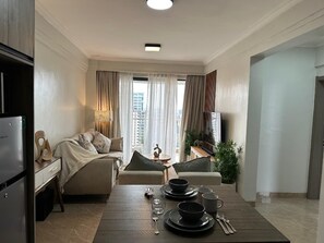 A modern hotel room with a dining area, a sofa set, a television, and a view of the cityscape. - Padmore Residences Kilimani (Nairobi)