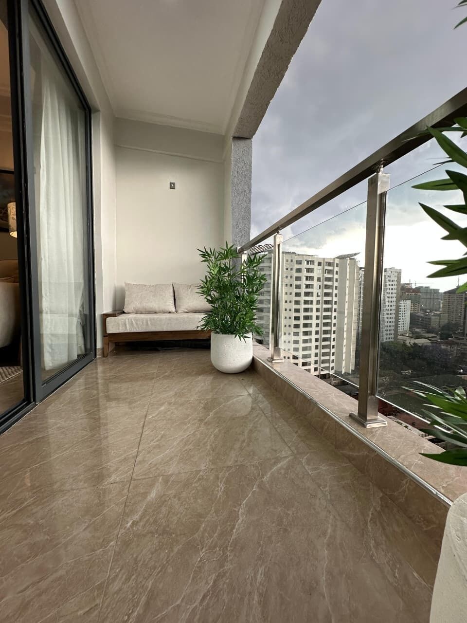 A balcony with a sofa, a potted plant, and a city view.