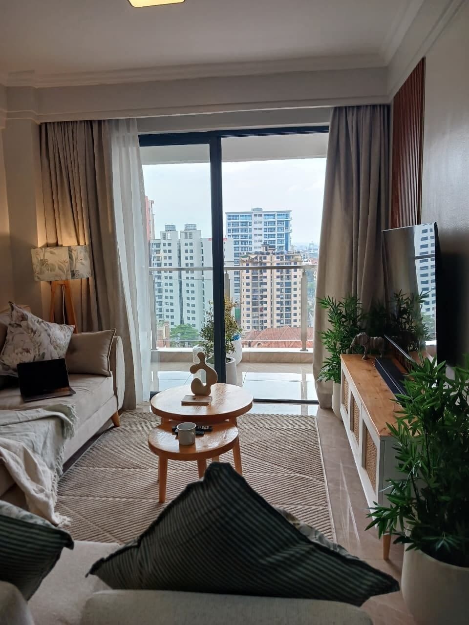 Una sala moderna con un sofá, una mesa de centro y un televisor. Tiene un balcón con vistas a edificios altos.
