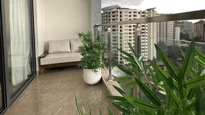 A balcony with a sofa, potted plants, and a view of high-rise buildings. - Padmore Residences Kilimani (Nairobi)