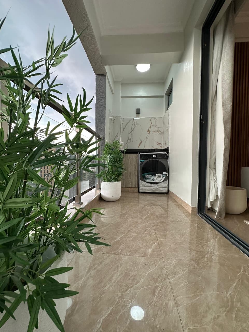 A balcony with a washing machine, potted plants, and a view of the city.