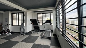 A gym with exercise equipment, a treadmill, and a window with a city view. - Padmore Residences Kilimani (Nairobi)