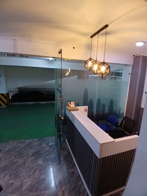 Zona de recepción con mampara de vidrio, mostrador de recepción y una silla azul.